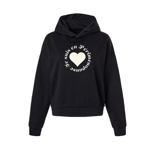 A black cropped pullover hoodie with a white graphic on the chest featuring a heart and circular text JE SUIS EN PÉRIMÉNOPAUSE, displayed on a solid white background.